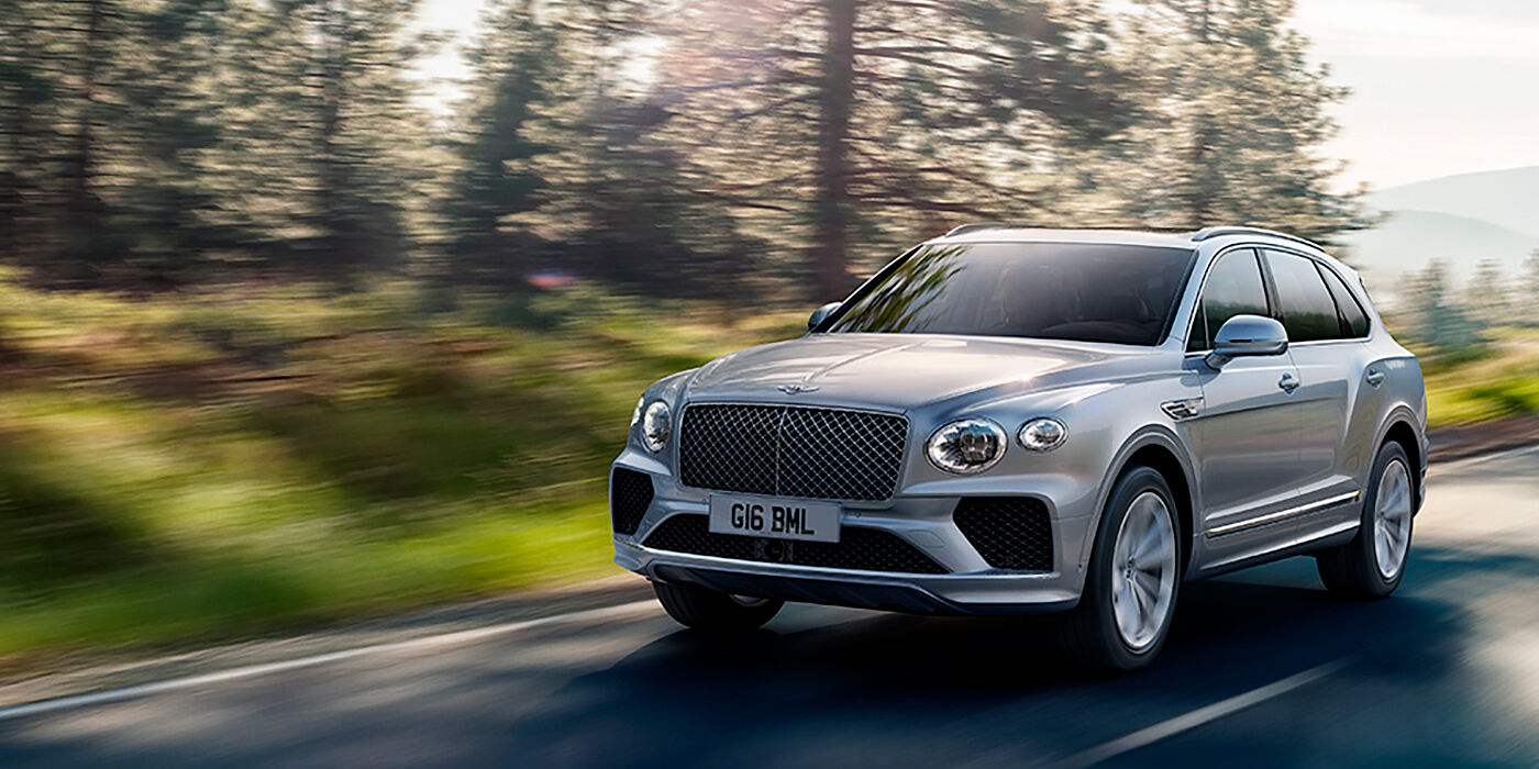 Bentley Seoul Bentley Bentayga luxury SUV front three quarter in Moonbeam paint, driving on an country road past trees.
